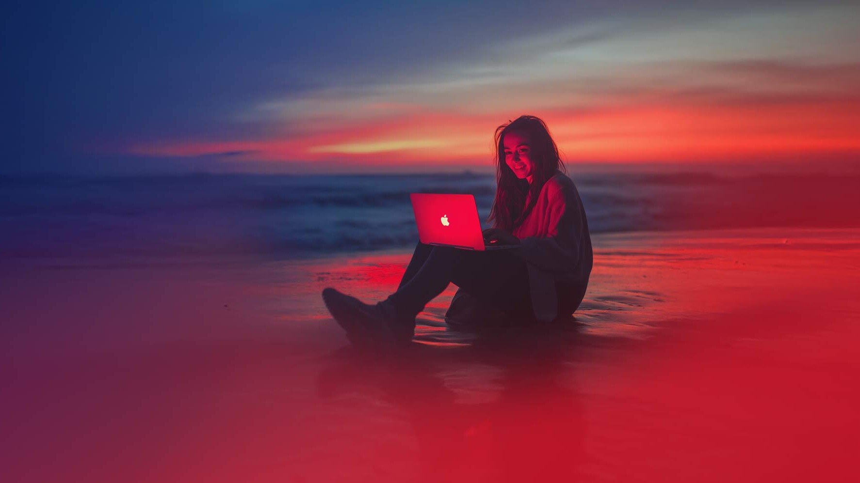 Woman on the beach at sunset with laptop.