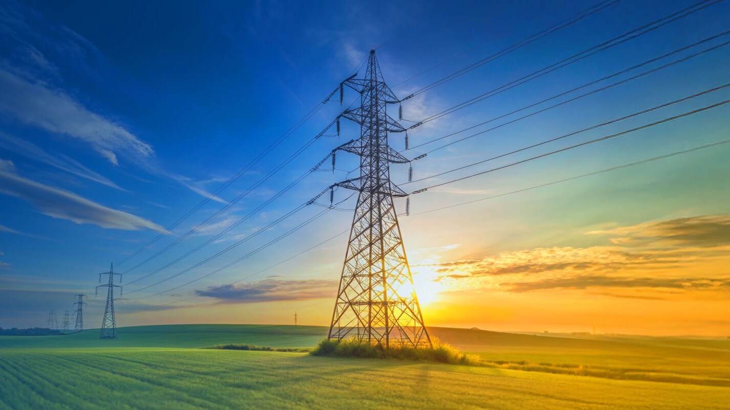 High-voltage power lines over a green field at sunset