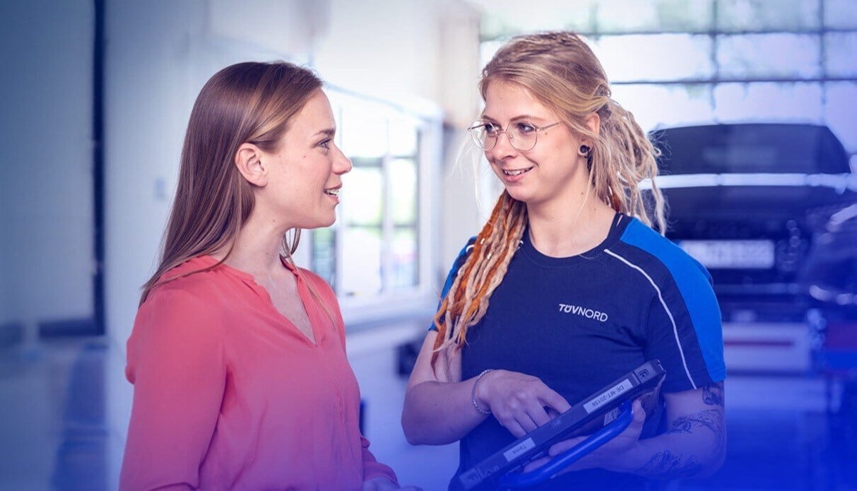 Two women are standing in a workshop. One woman is holding a tablet in her hands.