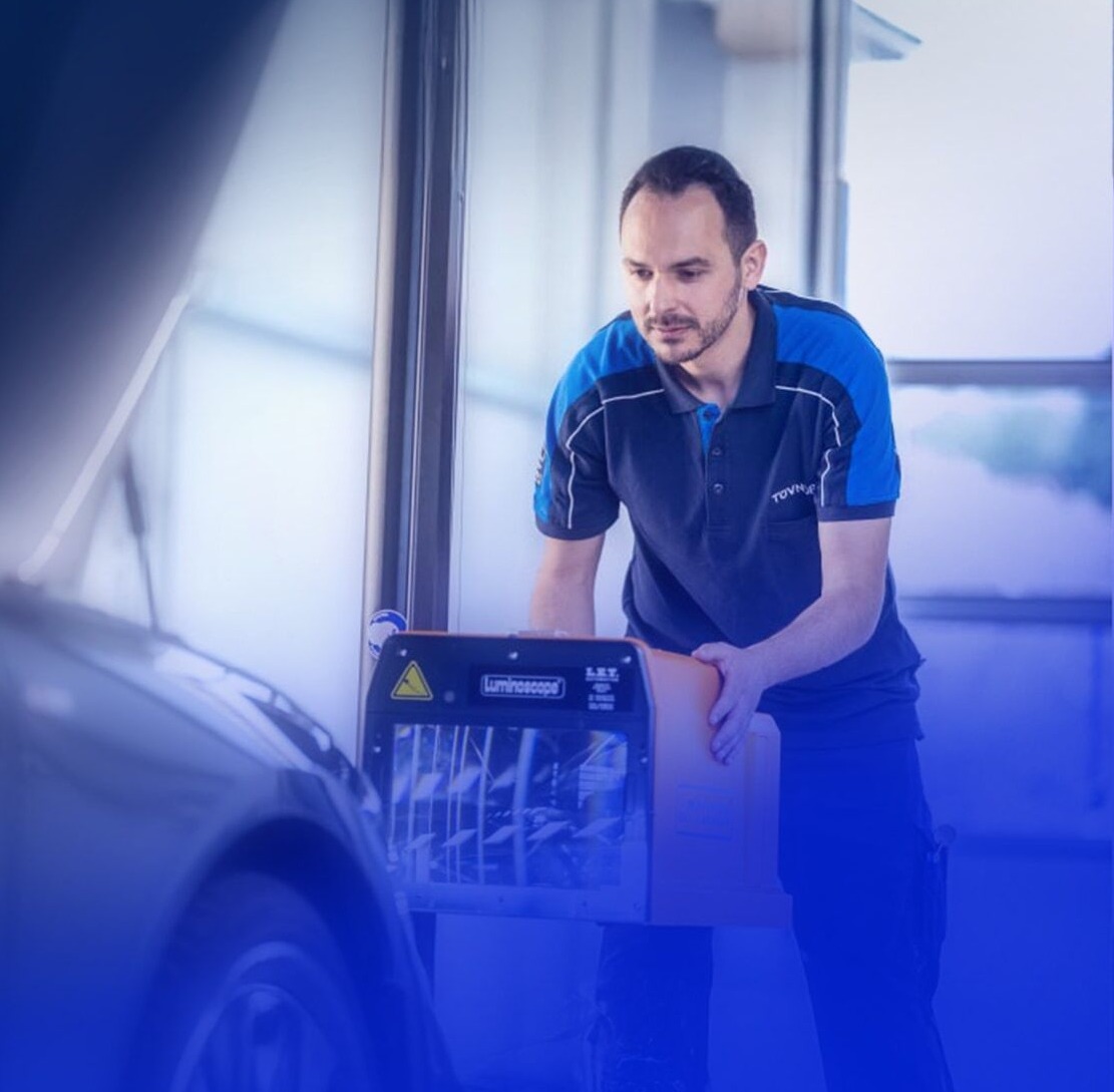 A man in a TÜV Nord shirt operates a diagnostic device in front of a vehicle.