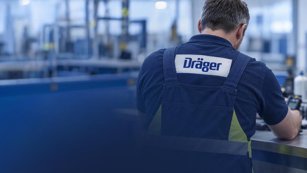 Person von hinten in Arbeitskleidung mit Dräger-Logo in einer Produktionshalle