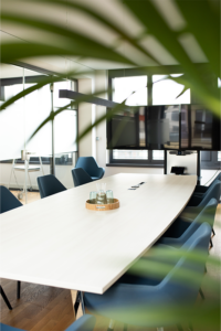 Meeting room with long table, surface hub and comfortable chairs in petrol. 