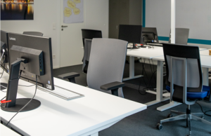 Photo with typical workplace with office chairs, tables and monitors.
