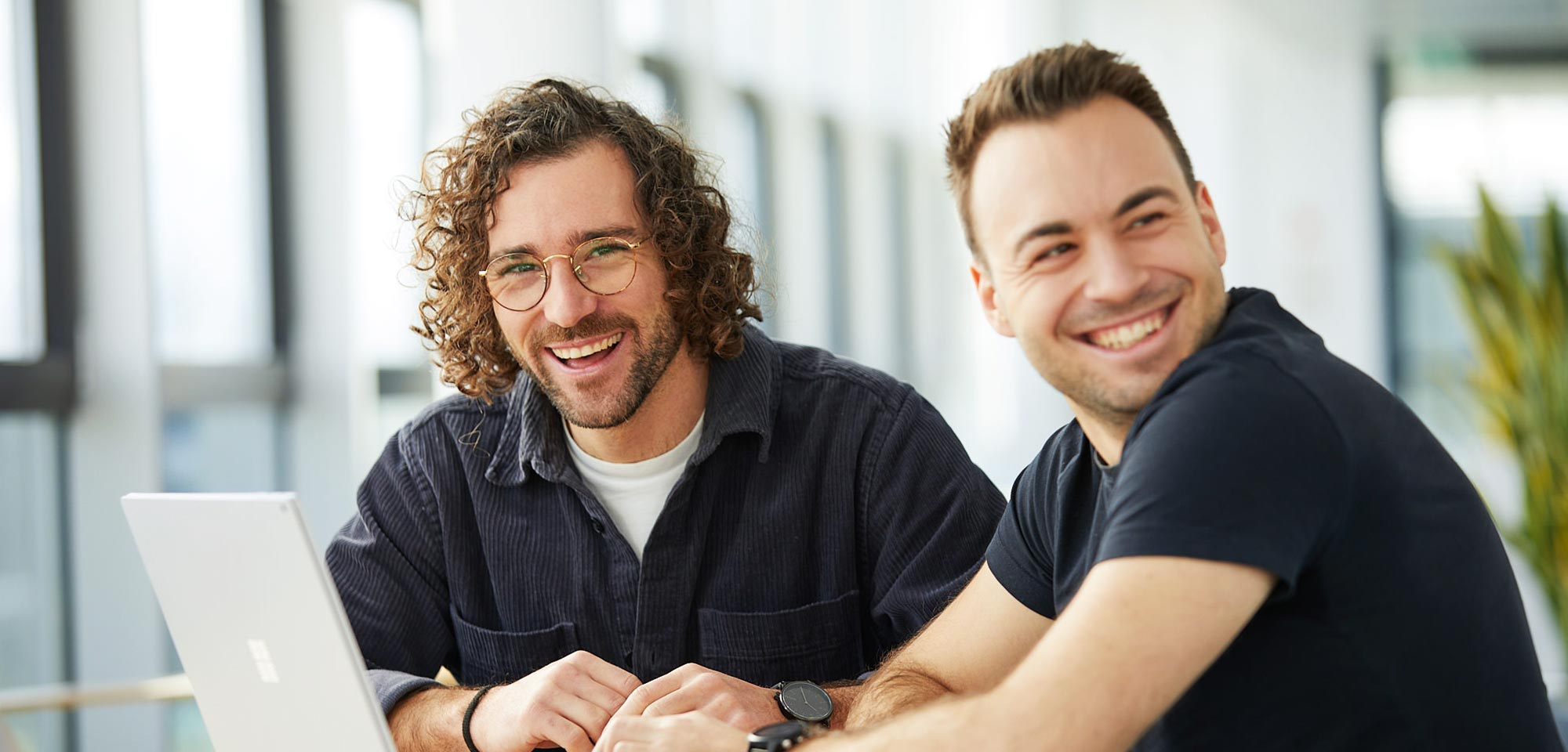 zwei Männer sitzen lachend vor einem Laptop