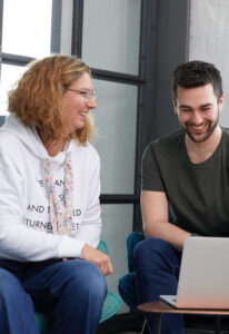 zwei Mitarbeitende vor einem Laptop, eine Frau im weißen Hoodie und ein Mann im T-Shirt