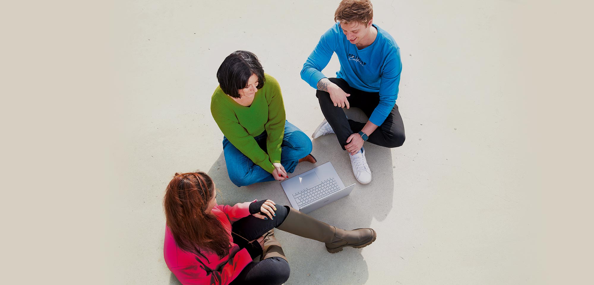 Mitarbeitende sitzen auf weißem Boden vor einem Laptop