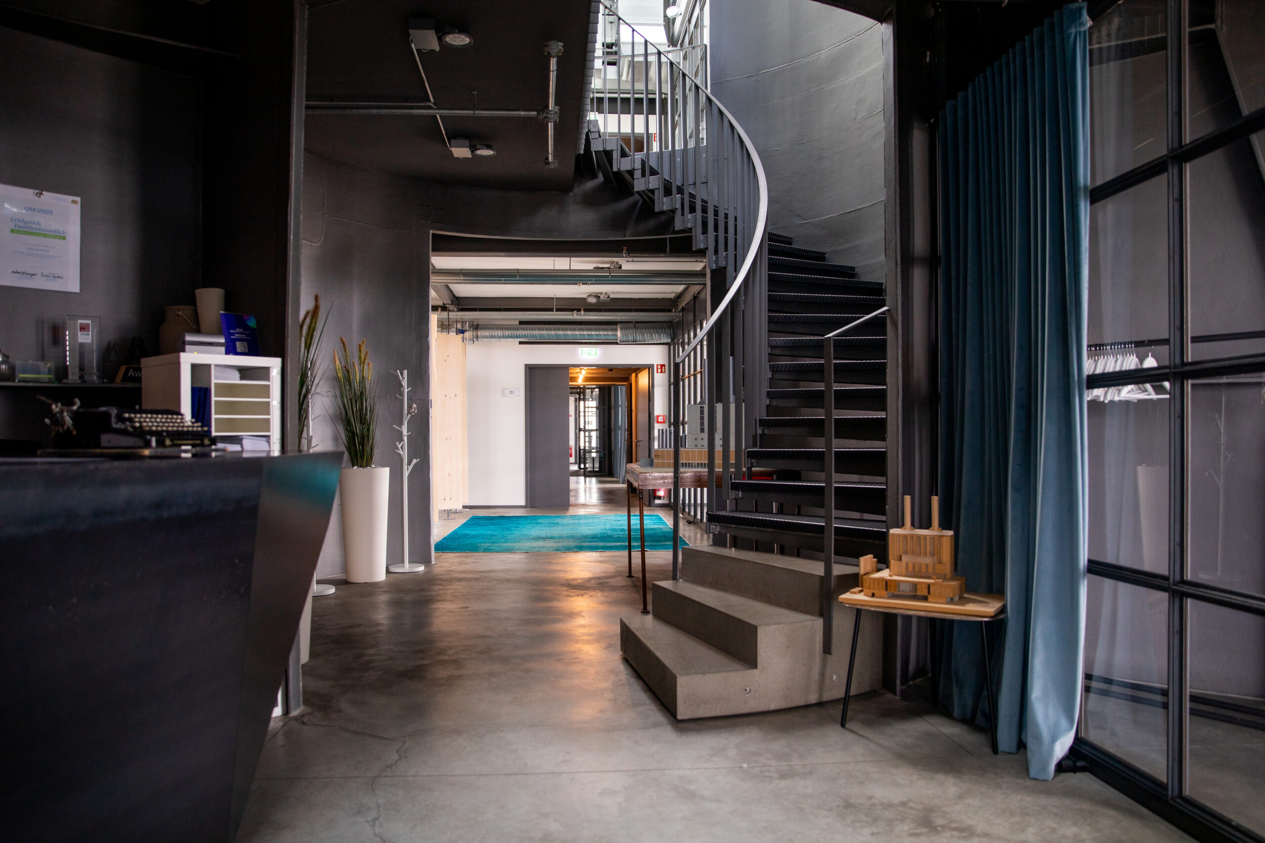 Photo showing the entrance to our Kraftwerk office in Munich. The ambience is loft-style. On the left you can see a counter, on the right a staircase leads up to another floor.