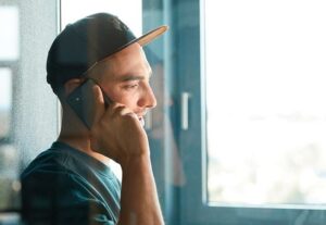 Young man with cap in side profile talking on cell phone.