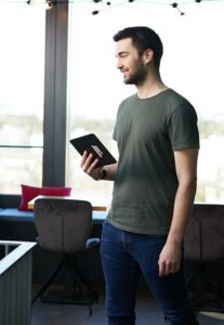 Young man in a green T-shirt with a friendly expression holds a notebook in his hand.