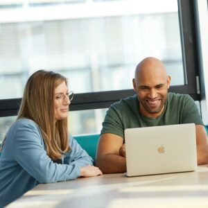 Mann mit lachendem Gesicht blickt mit einer Kollegin gemeinsam in einen Laptop.