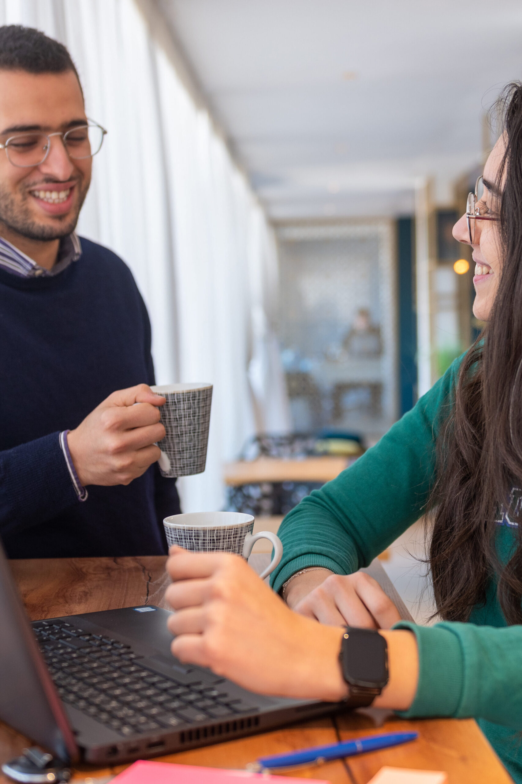 2 Personen trinken im Büro Kaffee vor einem Laptop