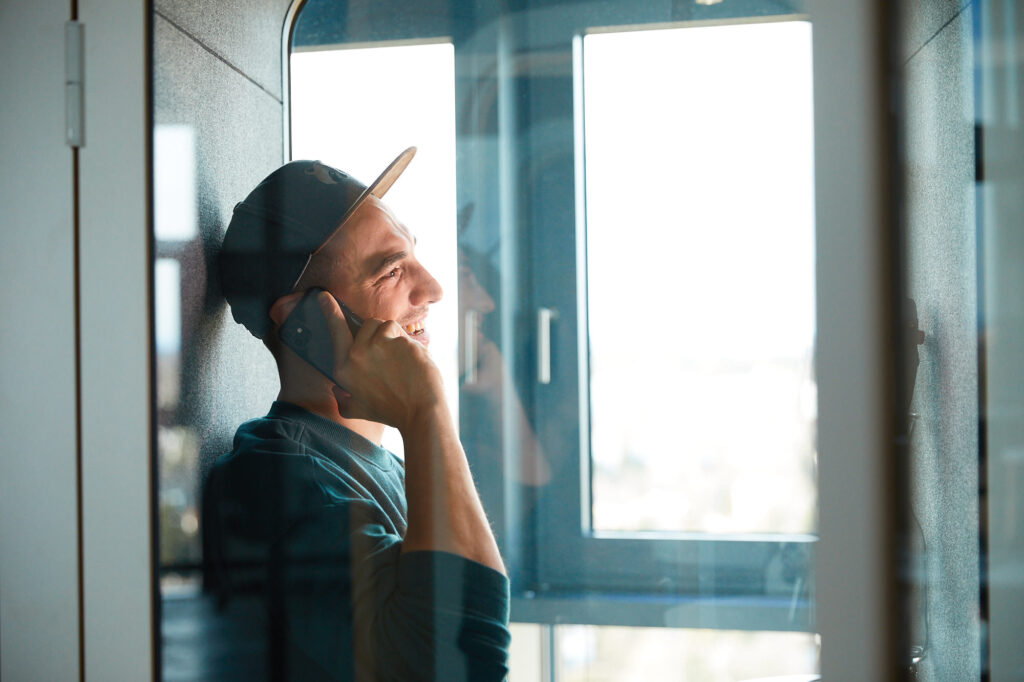 Mann steht in Telefonzelle und hält Handy ans Ohr