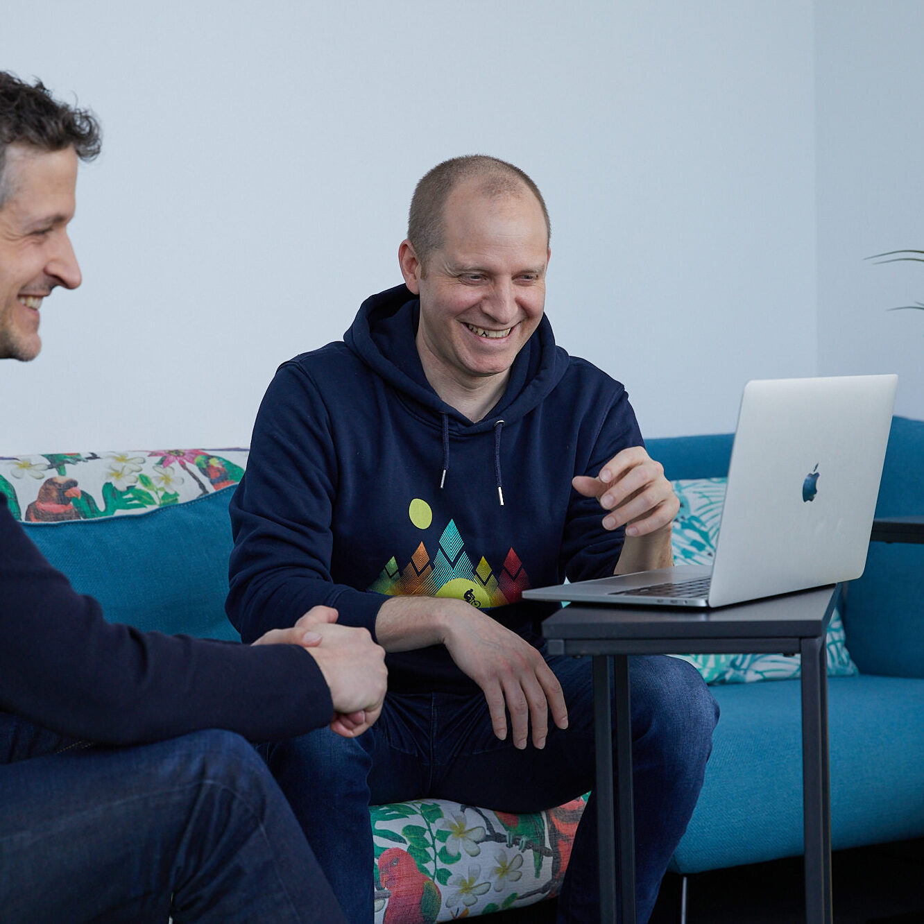 Lachende Kollegen sitzen auf dem Sofa vor einem Laptop