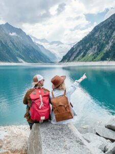 2 Menschen sitzen neben einem See mit Gebirgen im Hintergrund