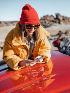 Junge Frau mit einem Handy neben einem Auto